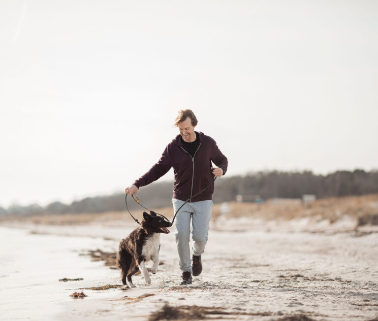 Middle aged caucasian man jogging and exercising on a beach with his border collie dog